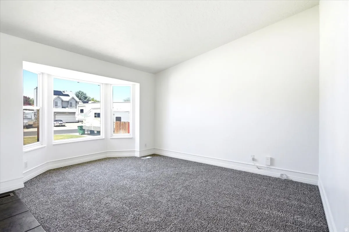 Bright interior space featuring a bay window, plush gray carpeting, white walls, and white baseboards