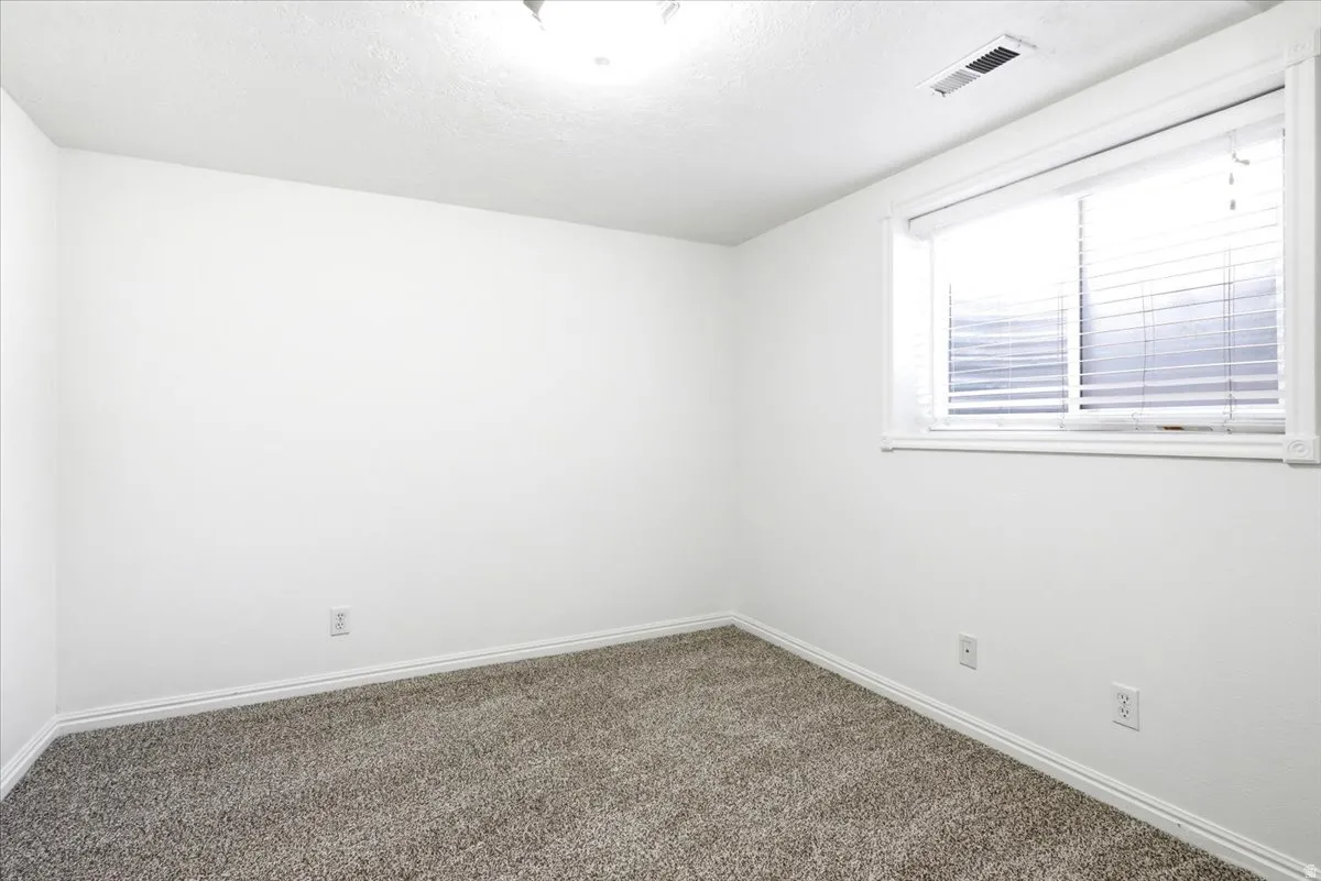Carpeted room featuring a window with horizontal blinds, white walls, and white baseboards