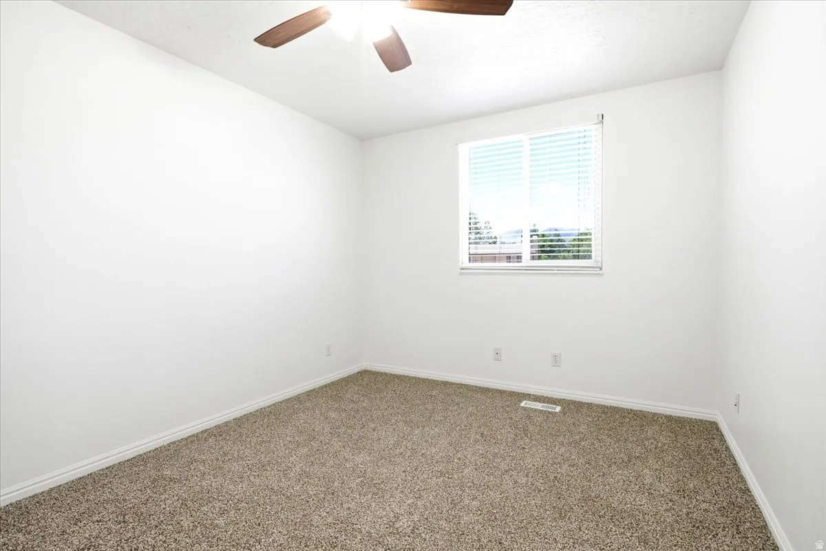 Carpeted room with a window featuring horizontal blinds, a ceiling fan with integrated lighting, white walls, and white baseboards