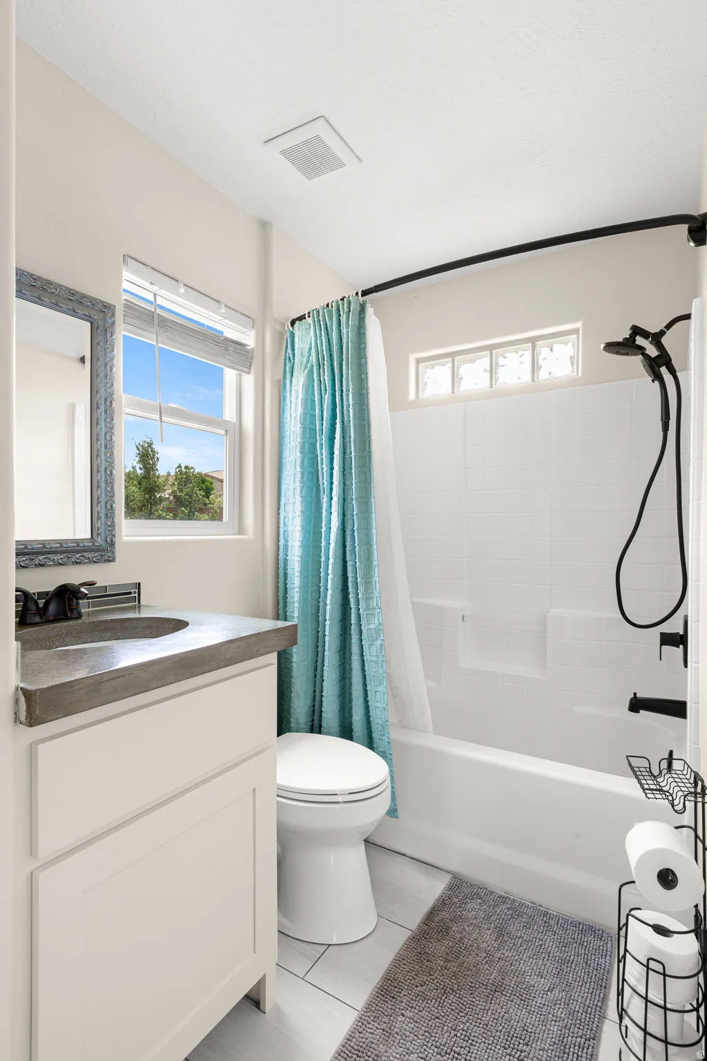 Bathroom featuring a modern vanity with a dark countertop and vessel sink, white cabinetry, a large window, a tub/shower combination with black fixtures, and light-toned tile flooring