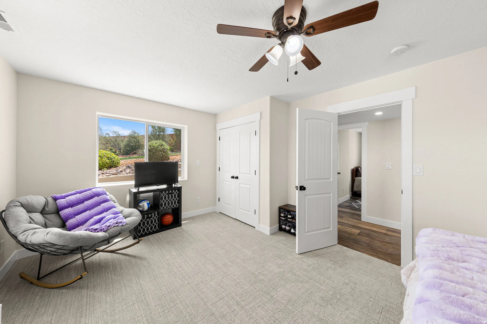 Carpeted room featuring a ceiling fan with light, a window with outdoor scenery, and two white paneled doors