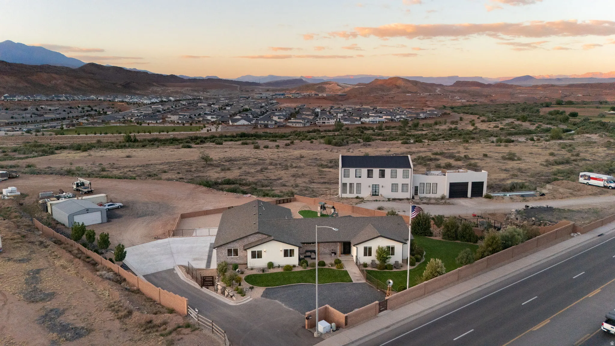 Expansive property featuring a single-story residence with a stone and stucco exterior, a two-story residence with a modern white facade and attached garages, a paved driveway, and established green lawn areas
