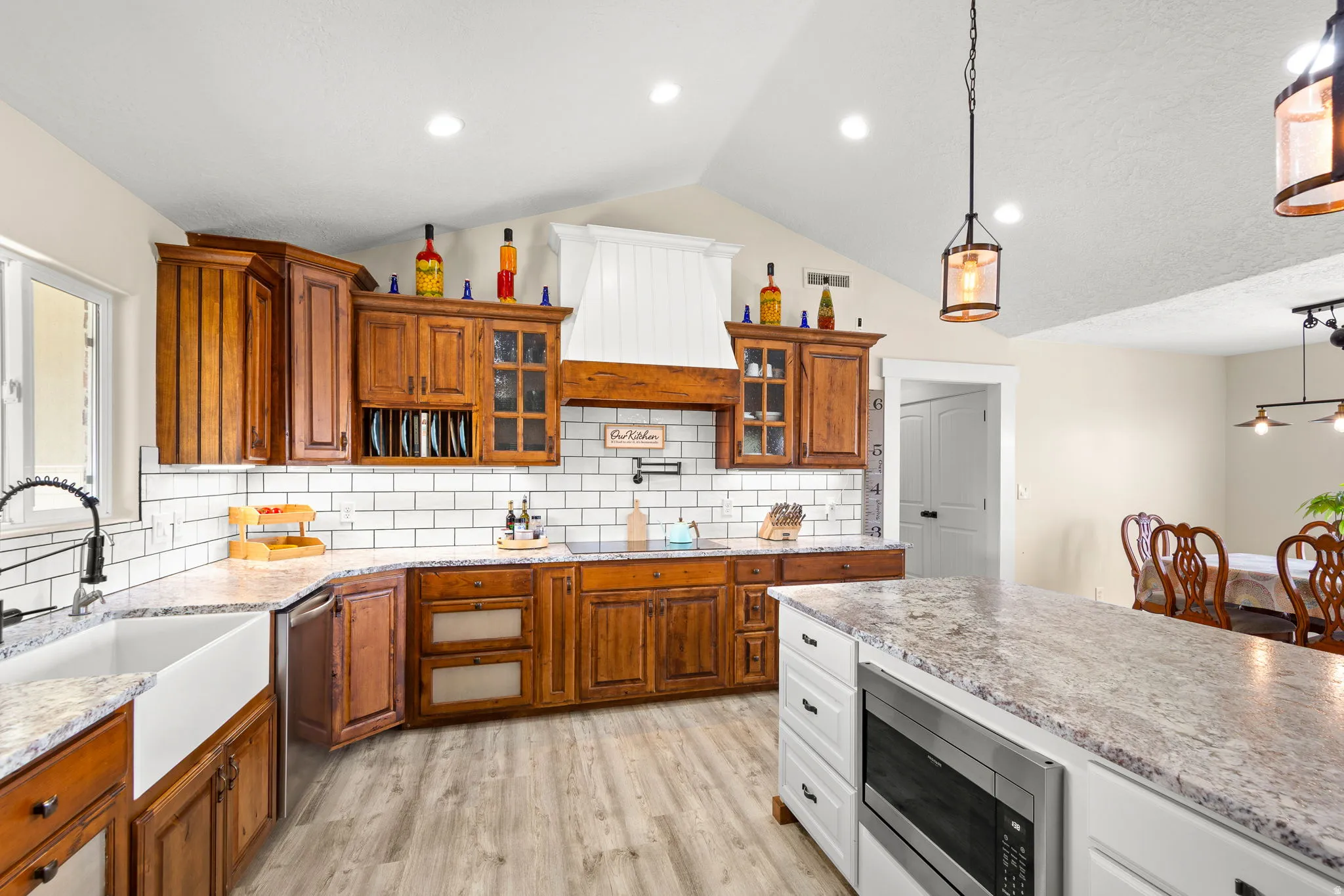 Kitchen featuring wood cabinetry, white subway tile backsplash, light-toned countertops, a farm sink, and an integrated microwave in the island