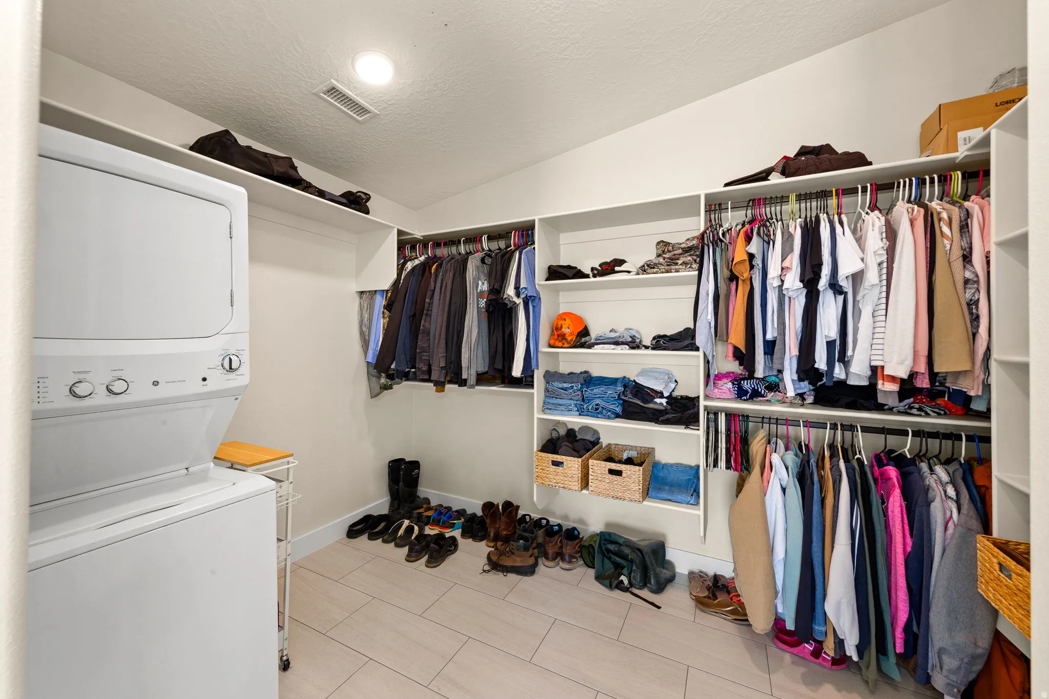 Integrated laundry closet with stacked appliances, featuring an organized walk-in closet with extensive built-in shelving, multiple hanging rods, and light wood-finish flooring