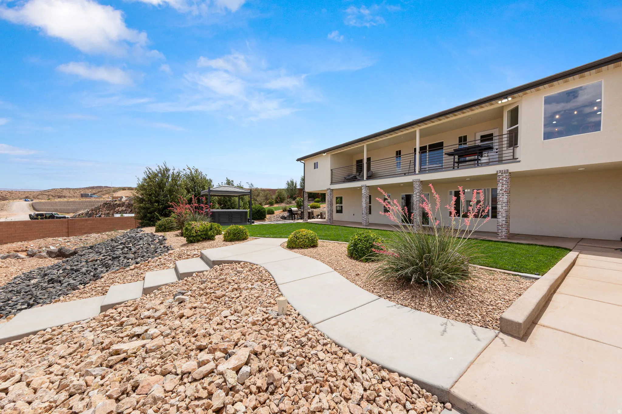 Rear exterior featuring an upper-level balcony with metal railings, a lower-level patio, and stone veneer support columns