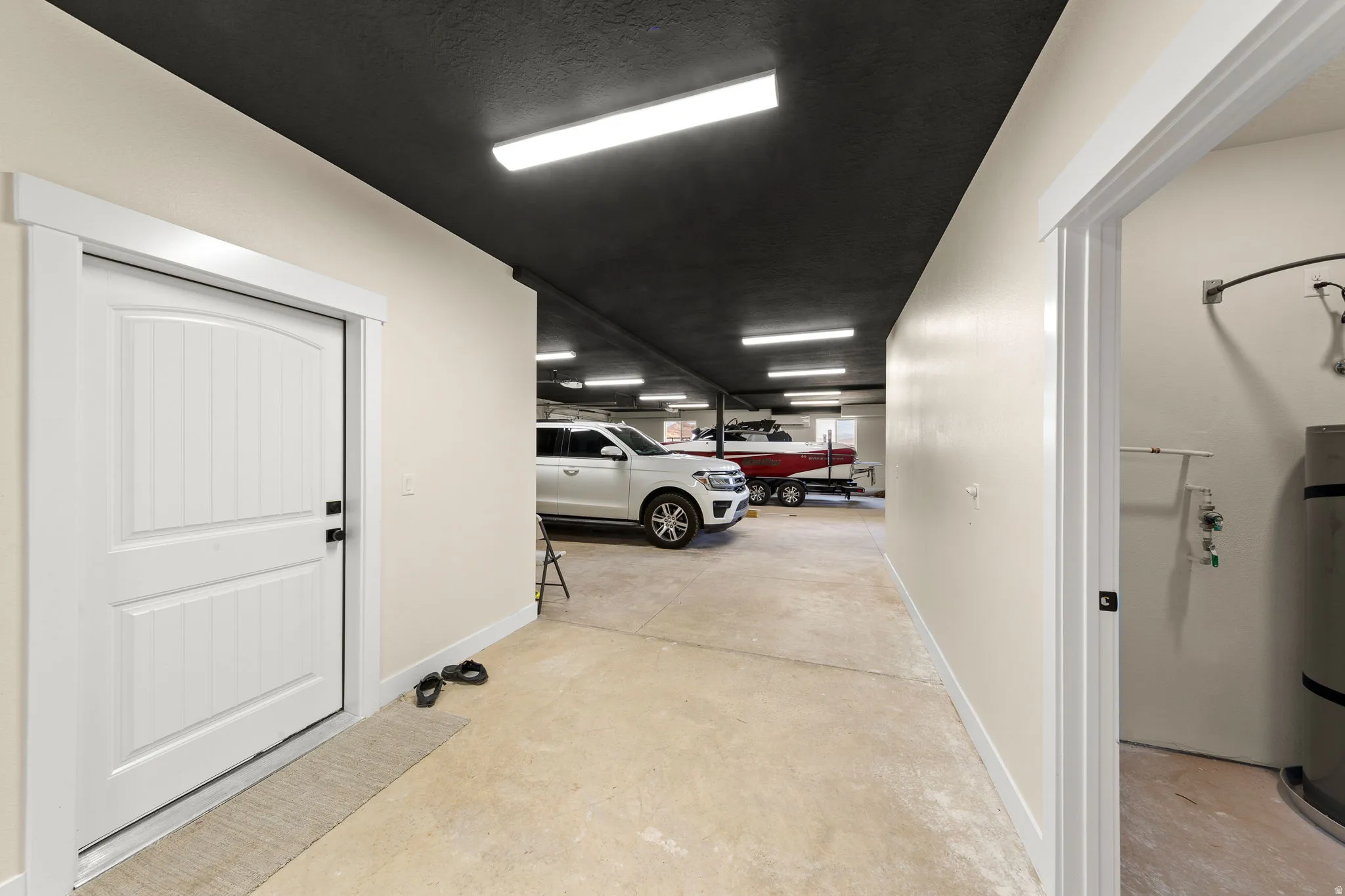 Large garage space with light concrete flooring, white painted walls, and a black painted ceiling