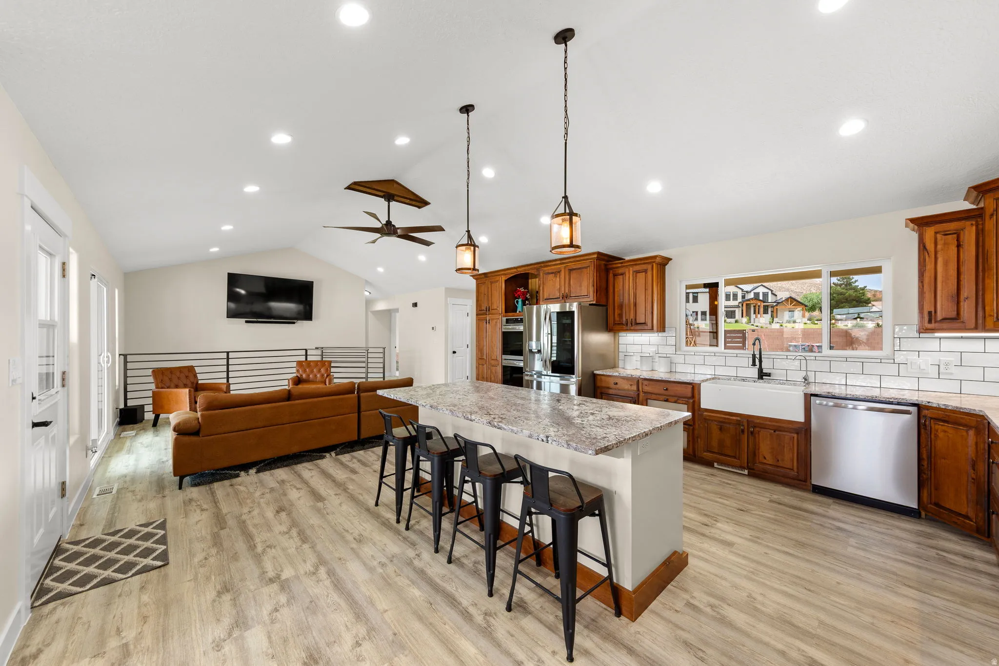 Spacious kitchen featuring an expansive island with seating, stainless steel appliances, a farmhouse sink, subway tile backsplash, and wood-finish flooring