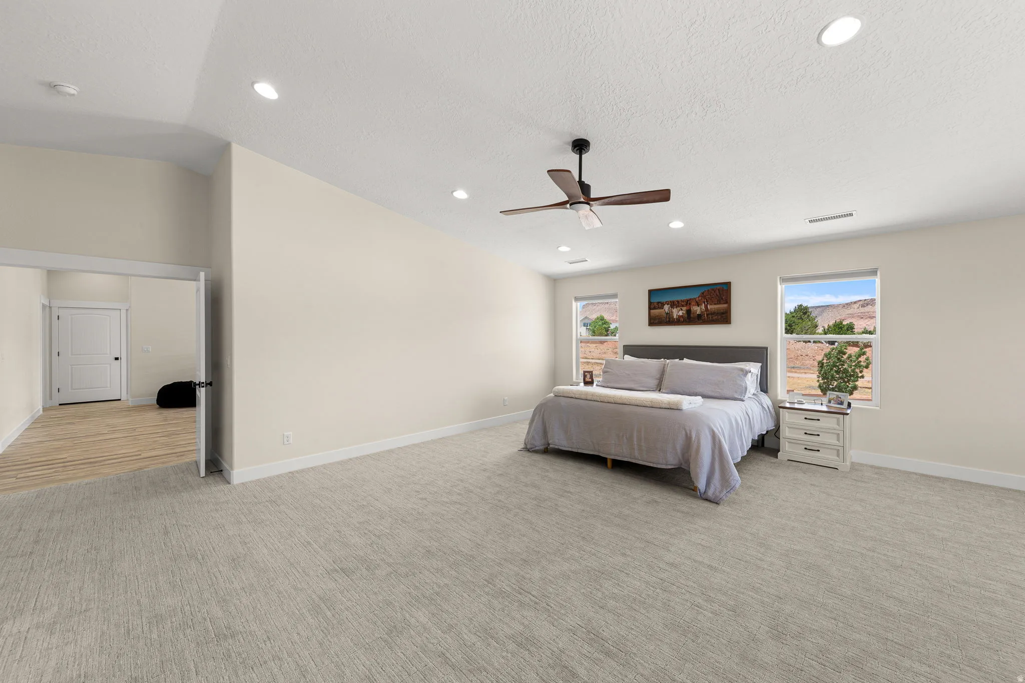 Spacious bedroom featuring light-colored walls, recessed ceiling lighting, and a dark wood-finish ceiling fan