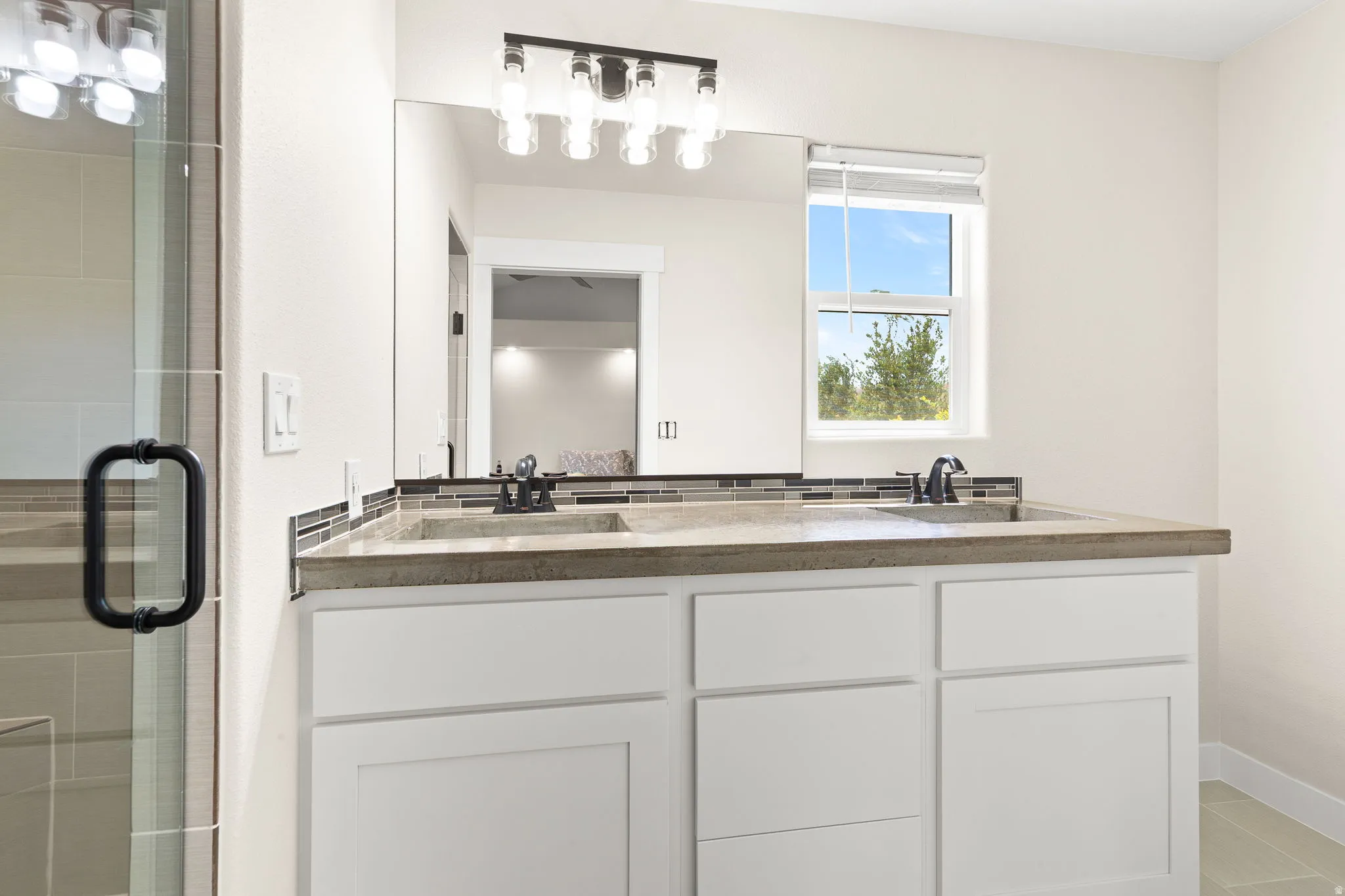 Dual-sink vanity featuring a light-toned countertop, mosaic tile backsplash, and matte black fixtures