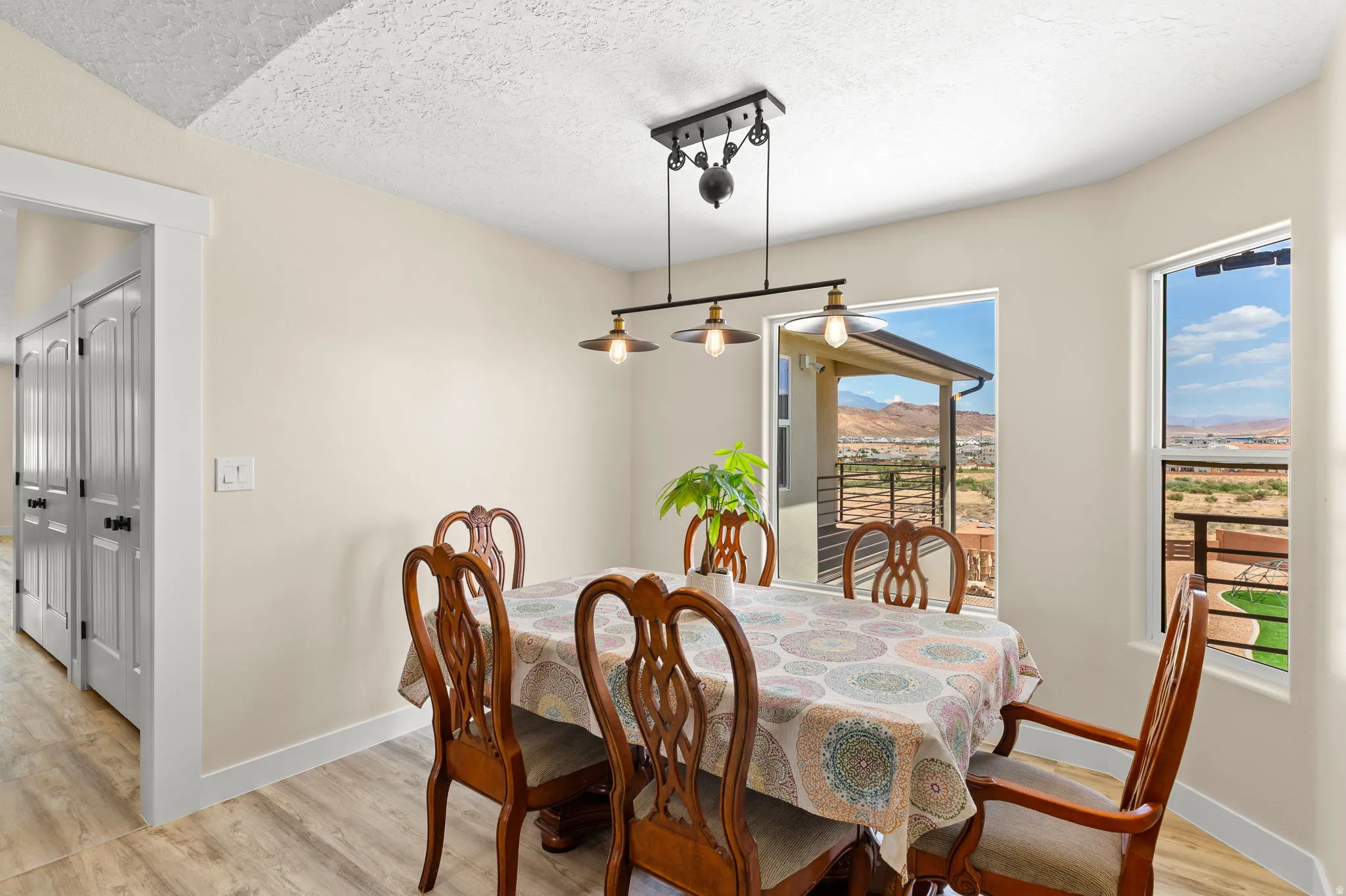 Dining area featuring a contemporary linear pendant light fixture, light wood-finish flooring, and multiple windows offering expansive territorial scenery