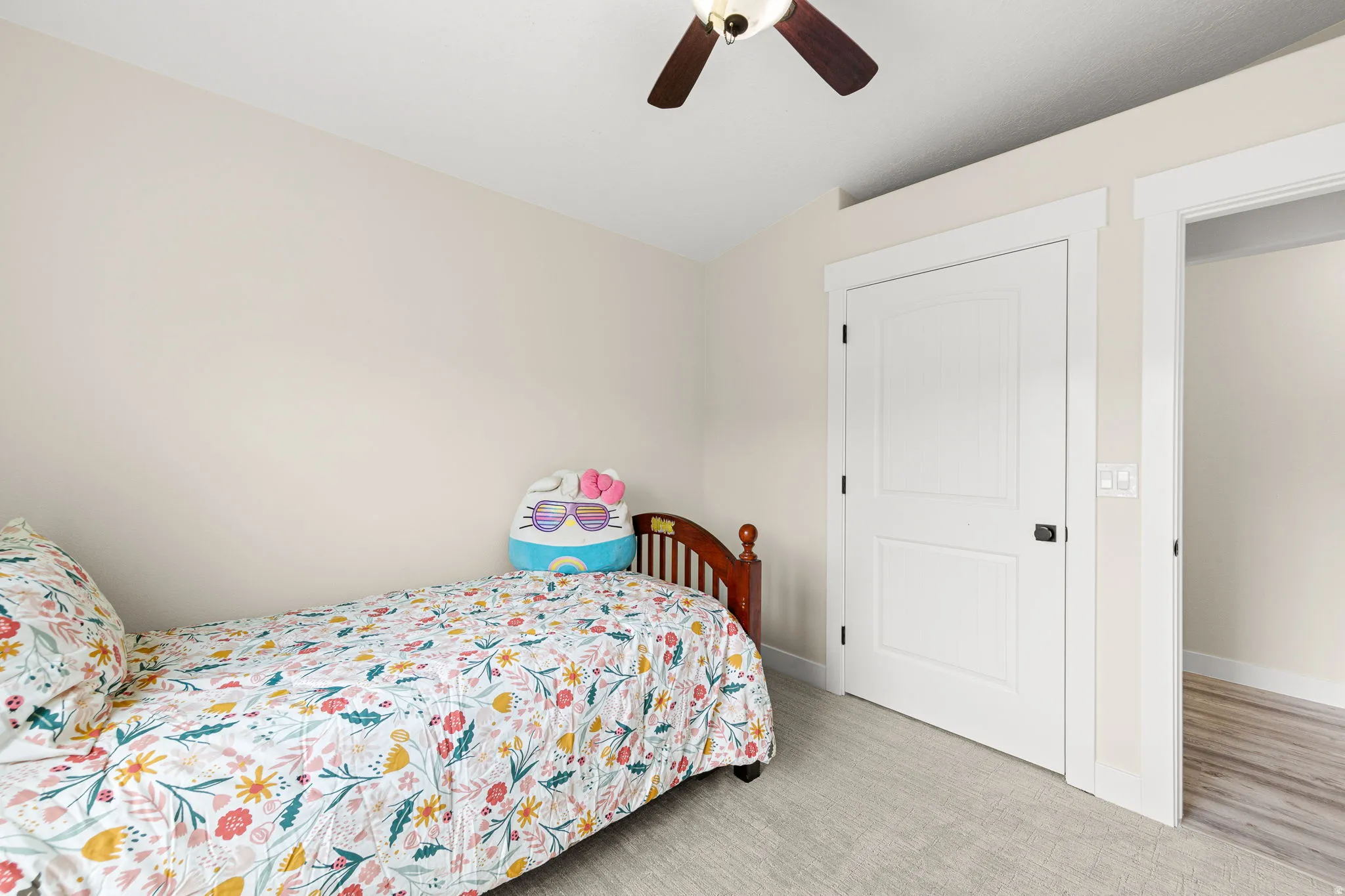 Carpeted room featuring a white two-panel door with black hardware, a ceiling fan with wood-finish blades, and neutral wall paint
