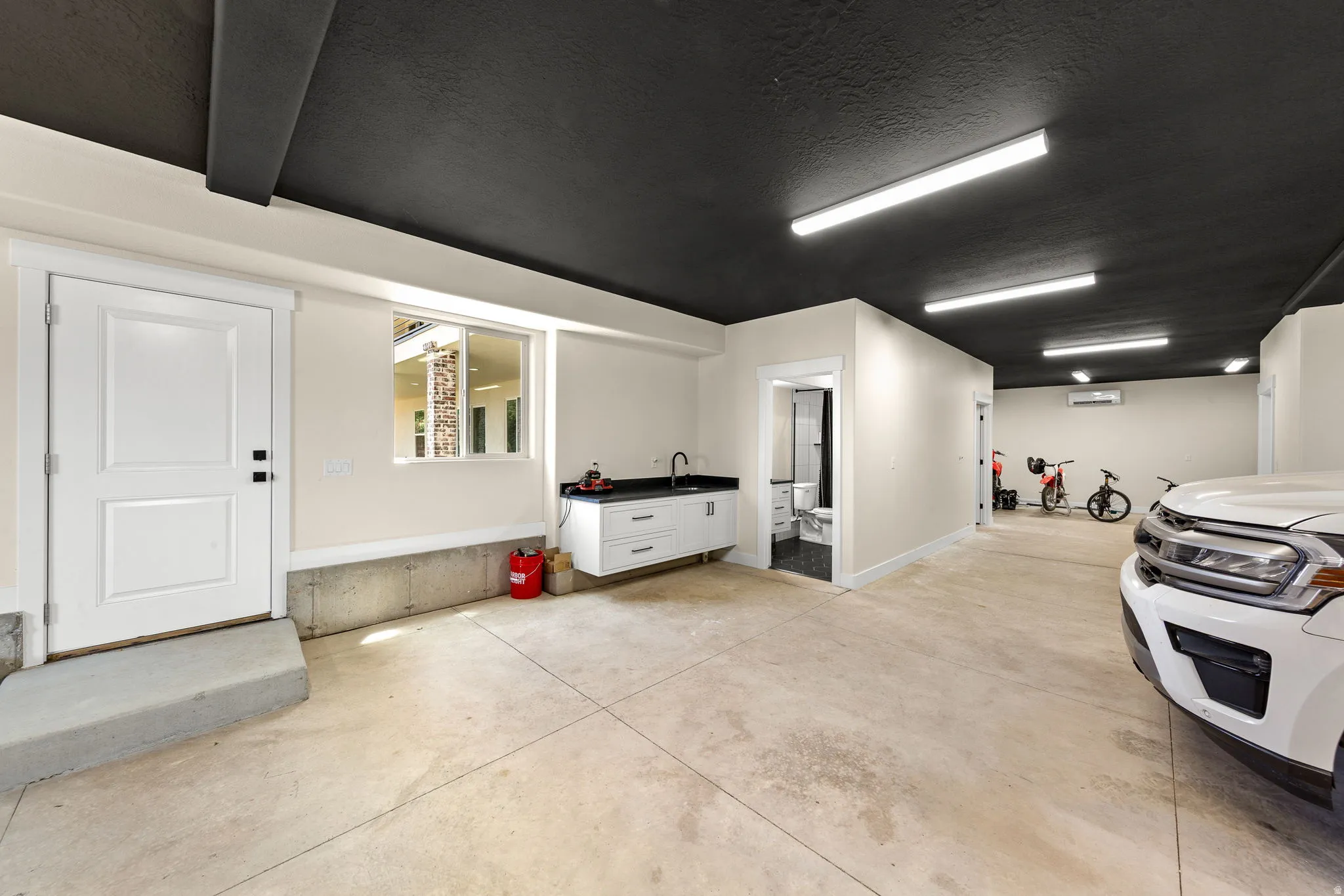Spacious garage featuring a dark ceiling, light-colored walls, concrete flooring, and multiple fluorescent light fixtures