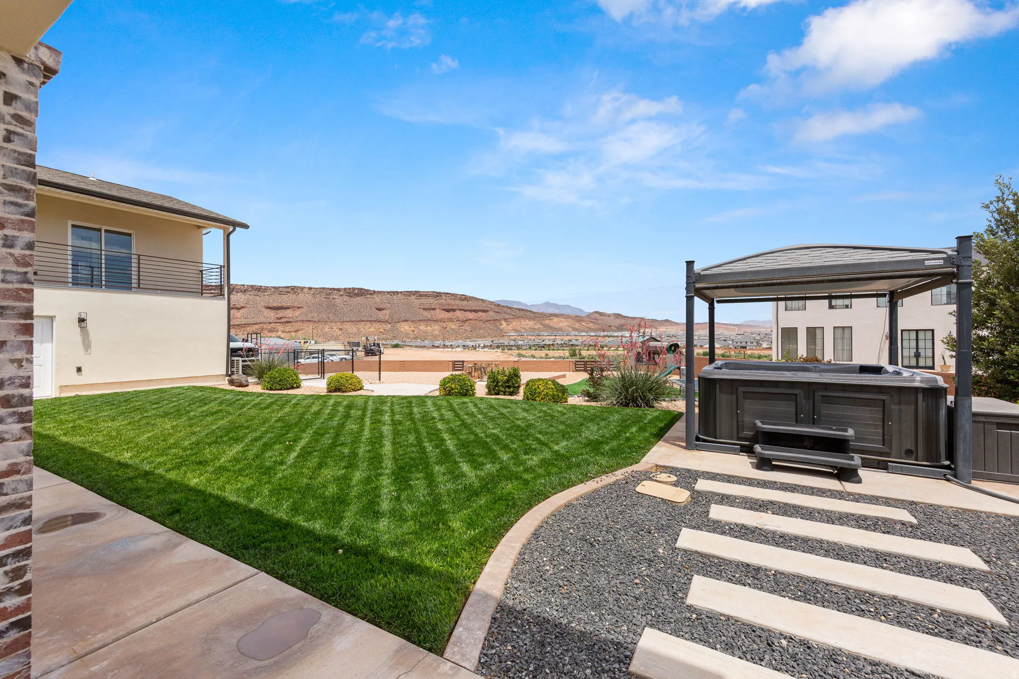 Expansive backyard featuring a hot tub with a pergola, a large manicured lawn, stone and concrete pathways, and a second-story balcony with metal railings