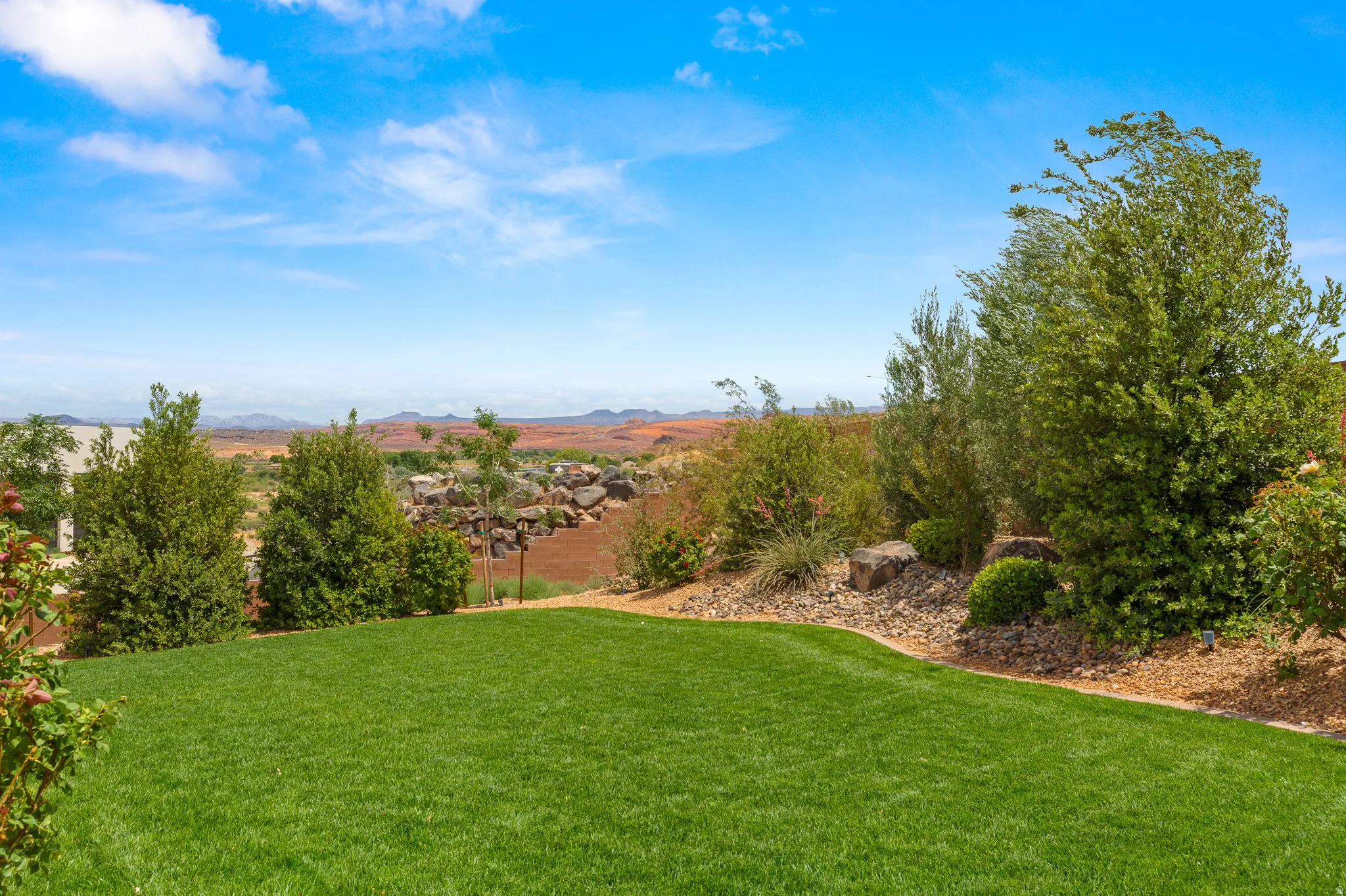 Expansive lawn area bordered by a rock and mulch landscape, featuring established trees and shrubs