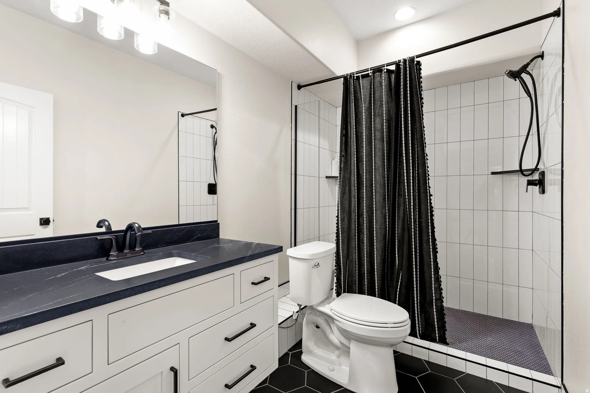 Bathroom featuring a white vanity with dark stone countertop, undermount sink, and matte black hardware