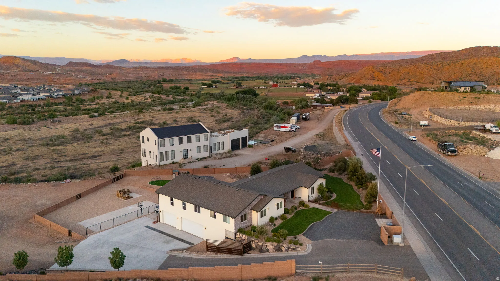 Two residences on an expansive property, featuring a modern white home with a dark roof and a traditional-style home with an attached garage