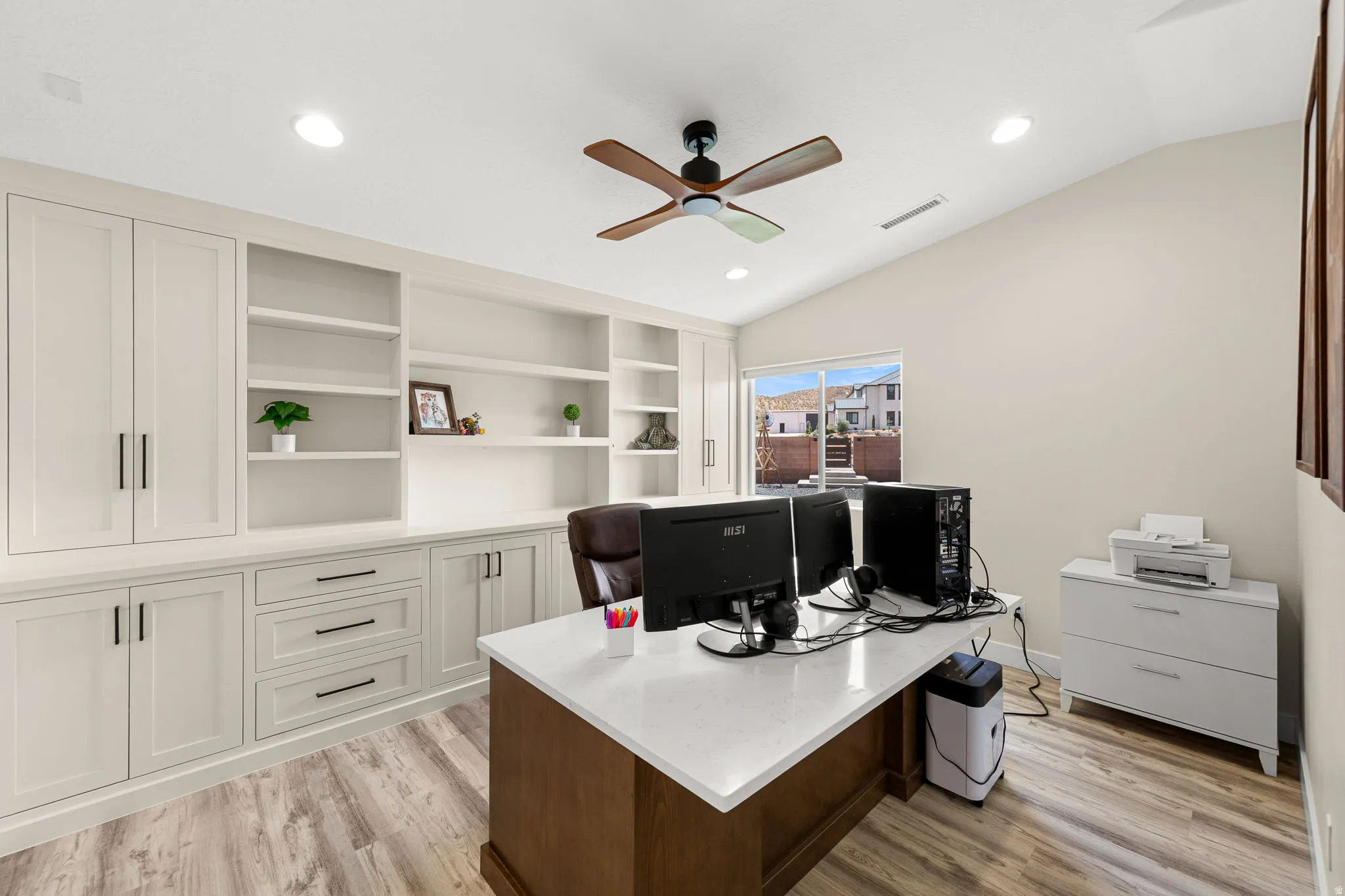 Dedicated office space featuring extensive built-in cabinetry, integrated shelving, wood-finish flooring, a vaulted ceiling, and recessed lighting