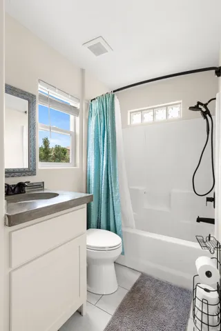 Bathroom featuring a modern vanity with a dark countertop and vessel sink, white cabinetry, a large window, a tub/shower combination with black fixtures, and light-toned tile flooring