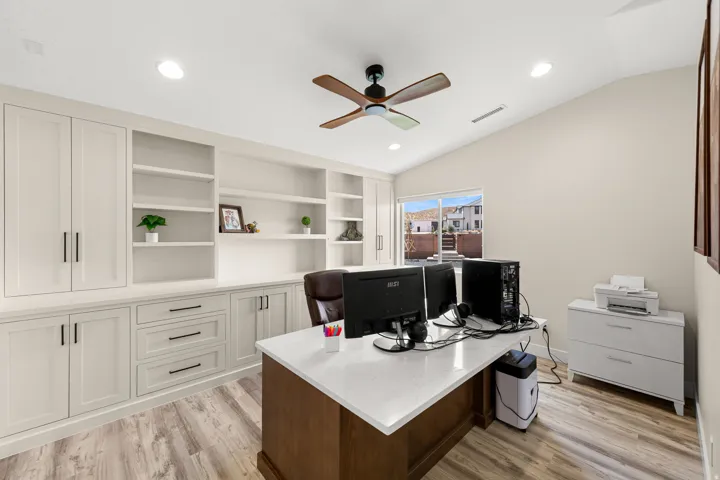 Dedicated office space featuring extensive built-in cabinetry, integrated shelving, wood-finish flooring, a vaulted ceiling, and recessed lighting
