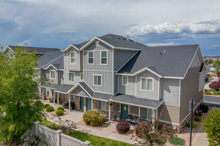 Multi-level townhome exterior featuring gray siding, stone accents, and dark shingle roofing