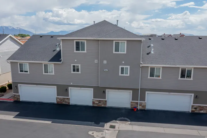 Multi-level townhome exterior featuring gray siding, white-trimmed windows, and multiple garage doors