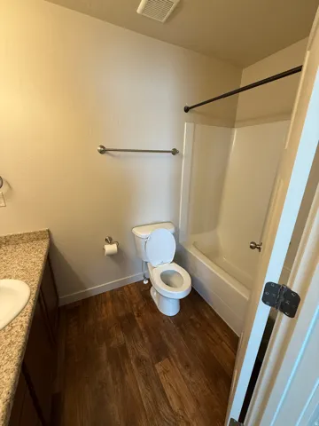 756-Bathroom featuring a white toilet, white bathtub with shower, wood-finish flooring, and a vanity with a speckled countertop