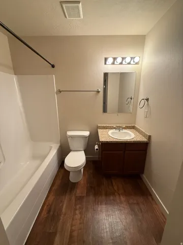 756-Bathroom featuring a white bathtub, wood-finish flooring, a vanity with a light-colored countertop and dark wood cabinetry, a mirror, and a wall-mounted light fixture