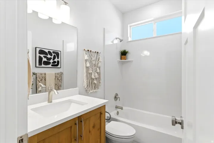 Bathroom featuring a wood-finish vanity with a white countertop and integrated sink, brushed nickel faucet, large mirror, and a full-size bathtub with a shower