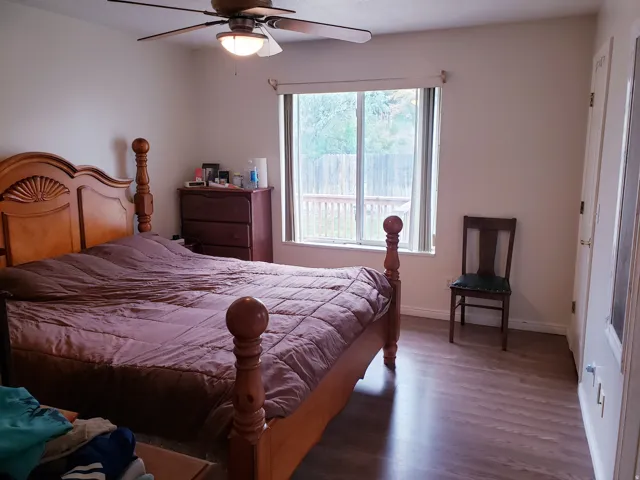 Bedroom featuring a ceiling fan with integrated lighting, wood-finish flooring, and a window overlooking an outdoor deck
