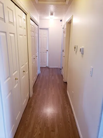 Hallway featuring wood-finish flooring, white walls, and white paneled doors