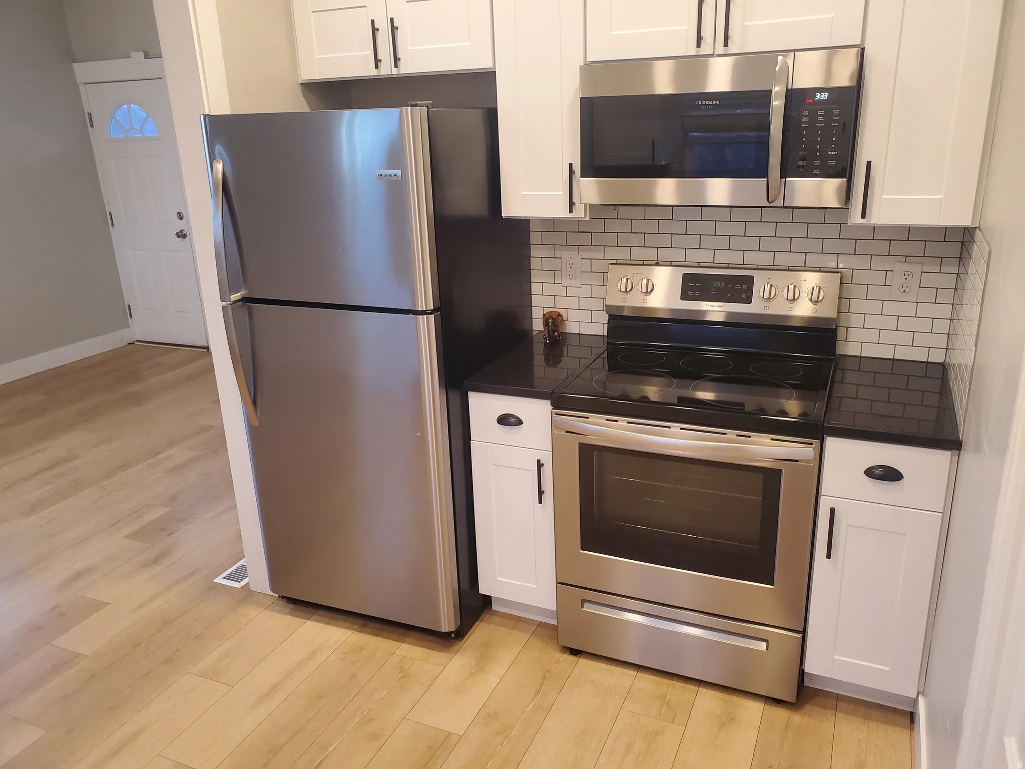 Kitchen featuring stainless steel appliances, white shaker-style cabinetry, black countertops, and a white subway tile backsplash