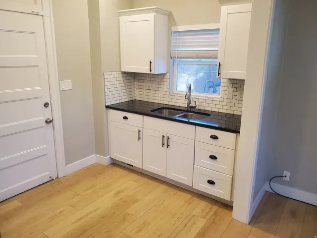 Modern kitchen area featuring white shaker-style cabinetry with matte black hardware, a black countertop, and a white subway tile backsplash