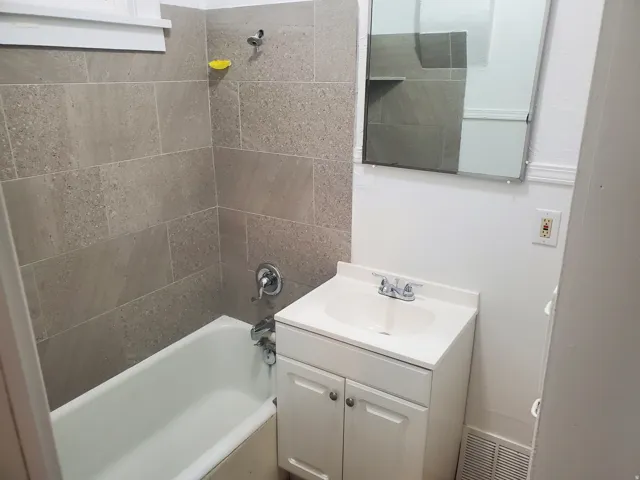Bathroom featuring a white bathtub, gray rectangular tile surround, chrome fixtures, white vanity with integrated sink, and a wall-mounted mirror