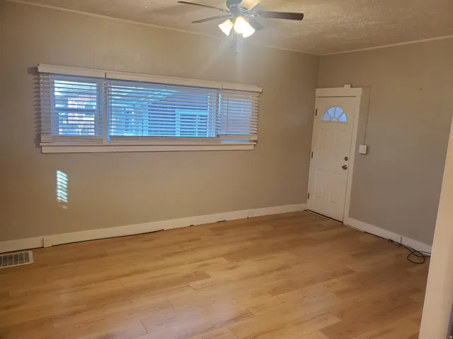 Living area featuring wood-finish flooring, neutral wall tones, a ceiling fan with integrated lighting, and a white entry door with an arched window insert