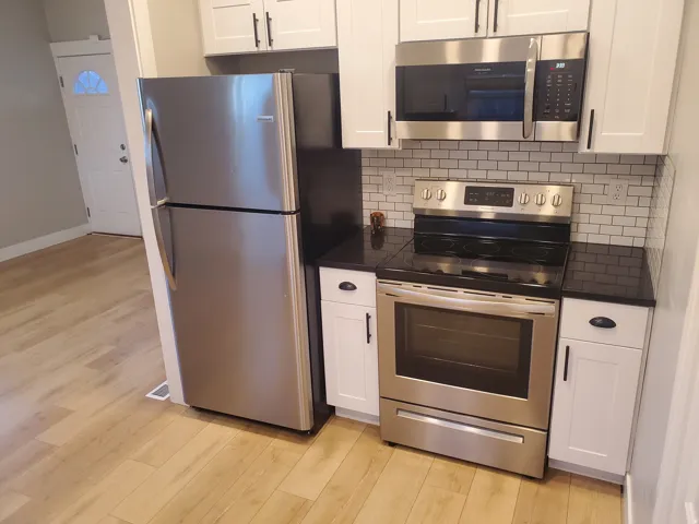 Kitchen featuring stainless steel appliances, white shaker-style cabinetry, black countertops, and a white subway tile backsplash