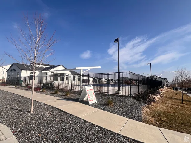 Exterior featuring a community pool area with black metal fencing, adjacent to a contemporary multi-story residence with a covered patio, and surrounded by gravel landscaping and a paved walkway