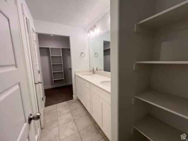 Bathroom featuring a double vanity with stone-finish countertop, ceramic tile flooring, and integrated lighting