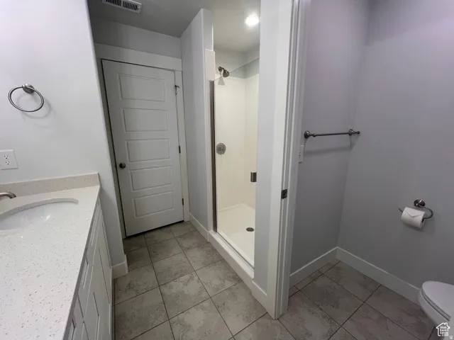 Contemporary bathroom featuring a walk-in shower with clear glass enclosure, a vanity with a white solid-surface countertop and integrated sink, and gray tile flooring
