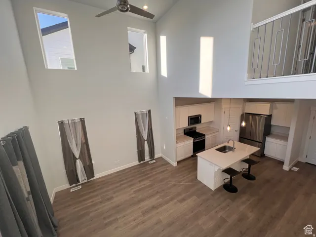 Open-concept living area featuring high ceilings, wood-finish flooring, a modern kitchen island with seating, stainless steel appliances, and a contemporary ceiling fan