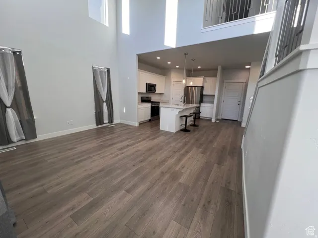 Open-concept living area featuring wood-finish flooring, high ceilings, and a kitchen with white cabinetry and stainless steel appliances