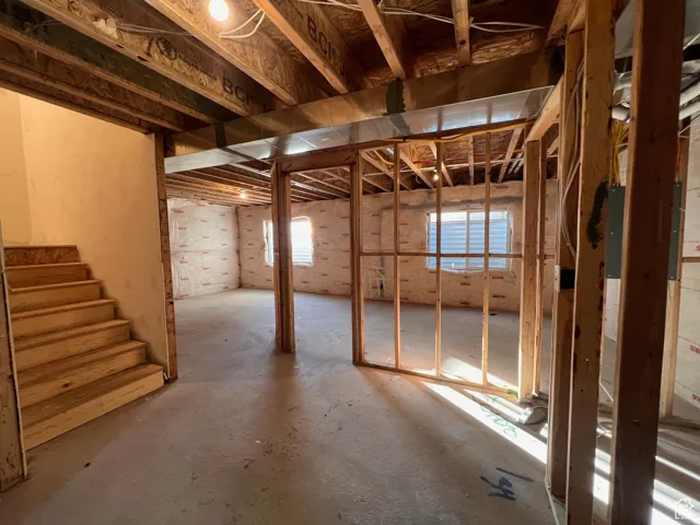 Unfinished basement space featuring exposed wooden joists, concrete flooring, and framing for future rooms