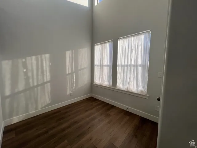 Room featuring high ceilings, wood-finish flooring, and multiple windows with sheer window treatments