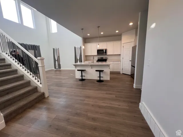 Spacious interior featuring wood-finish flooring, a contemporary kitchen island with pendant lighting, white cabinetry, and stainless steel appliances