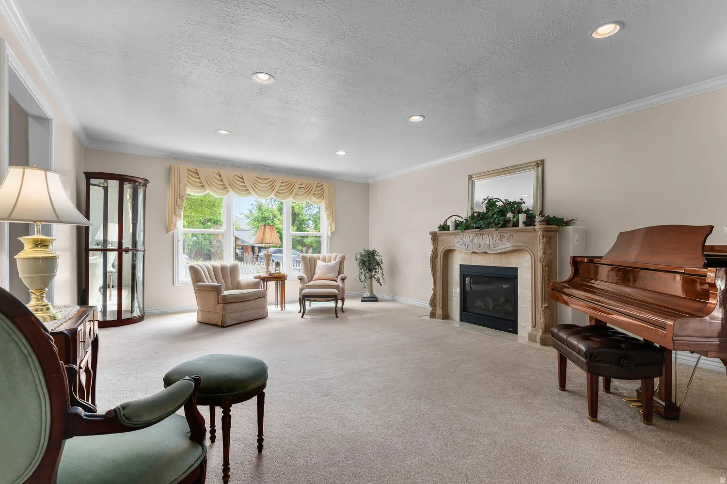 Spacious carpeted room featuring a decorative fireplace with an ornate mantel, large window with valance, recessed lighting, and crown molding