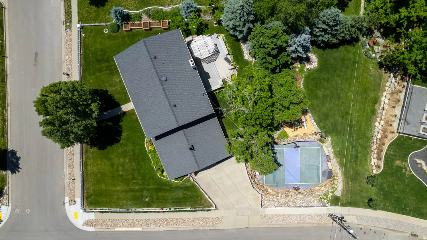 Expansive property featuring a multi-sport court, substantial green spaces, mature trees, and a tiered rock landscaping
