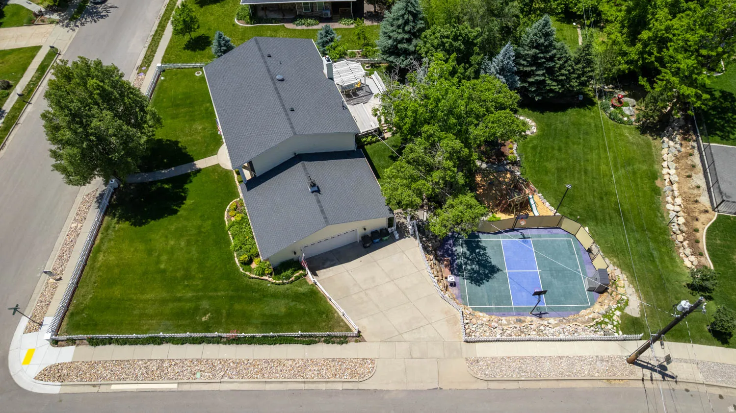 Expansive corner lot featuring a two-story residence with an attached garage, a dedicated sport court, and mature landscaping