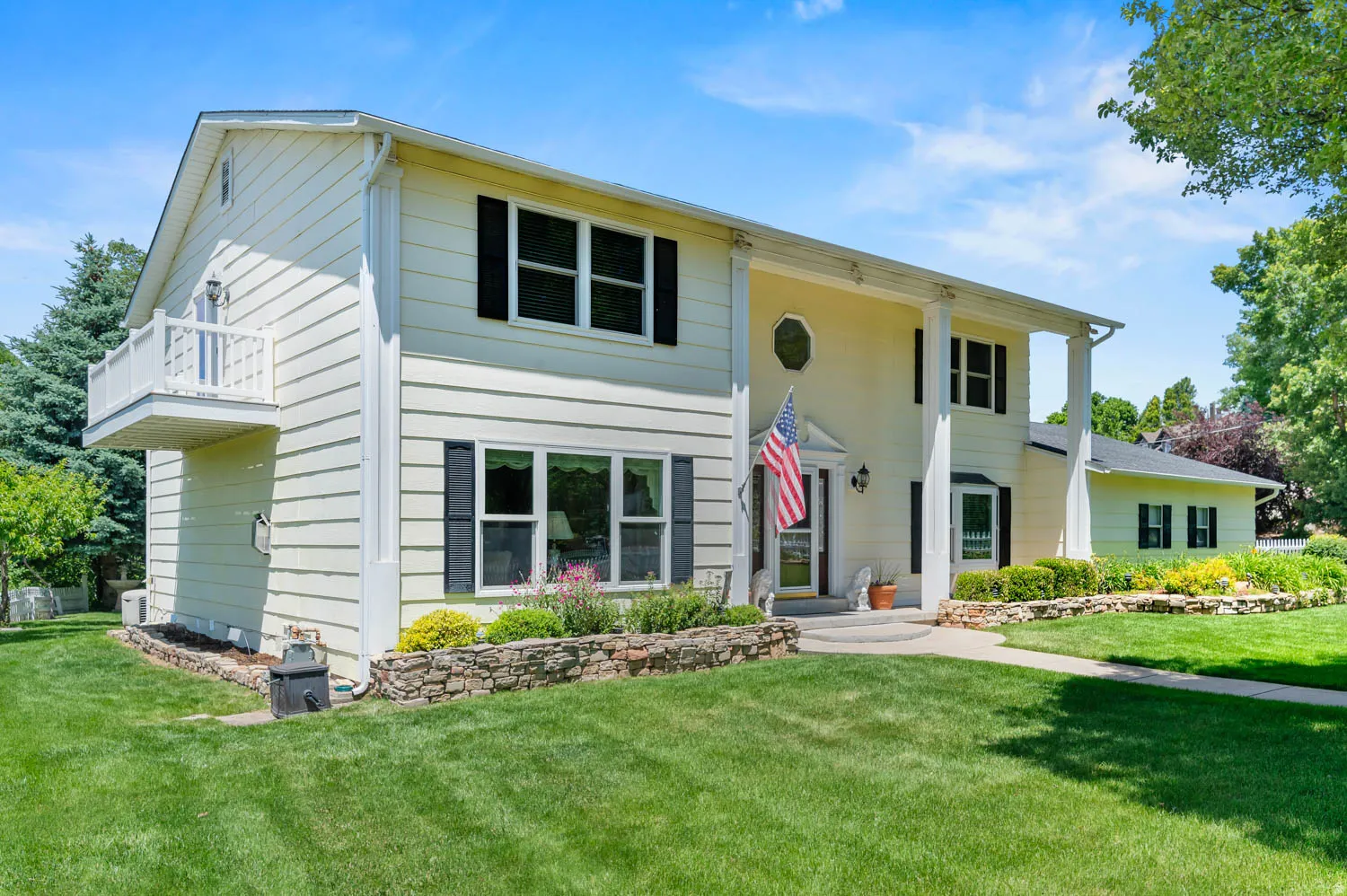 Classic two-story residence featuring a covered front entry with columns, a second-story balcony with white railing, and dark louvered shutters