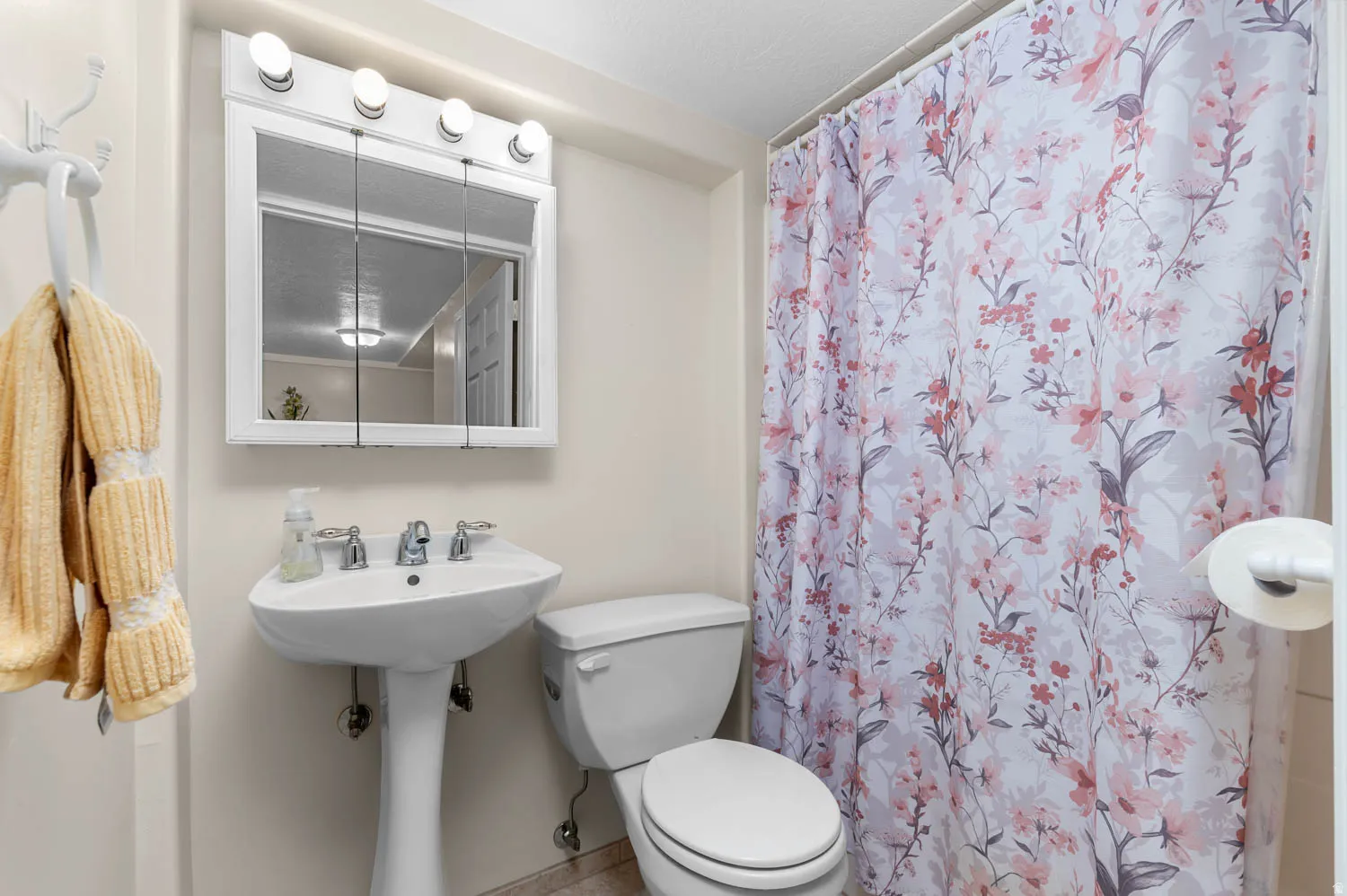 Bathroom featuring a white pedestal sink, dual-handle chrome faucet, and a wall-mounted medicine cabinet with integrated lighting