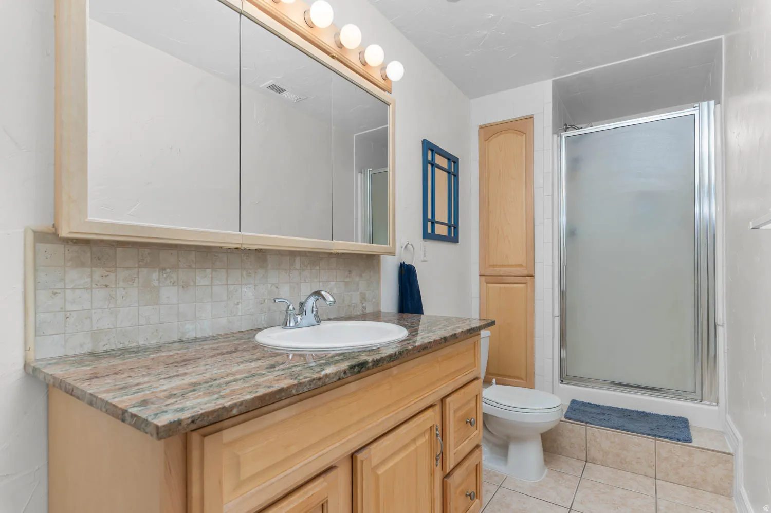 Bathroom featuring a light wood vanity with a stone countertop, an integrated sink, a chrome faucet, and a large mirrored medicine cabinet with overhead lighting