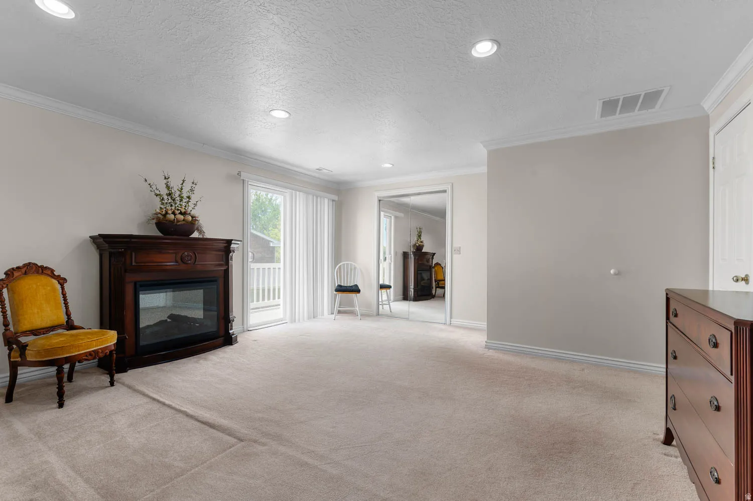 Spacious room featuring a decorative fireplace with dark wood surround, beige carpeting, recessed lighting, and crown molding